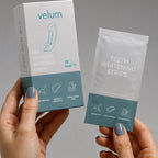 Manos sosteniendo la caja y el sachet de tiras blanqueadoras Velum